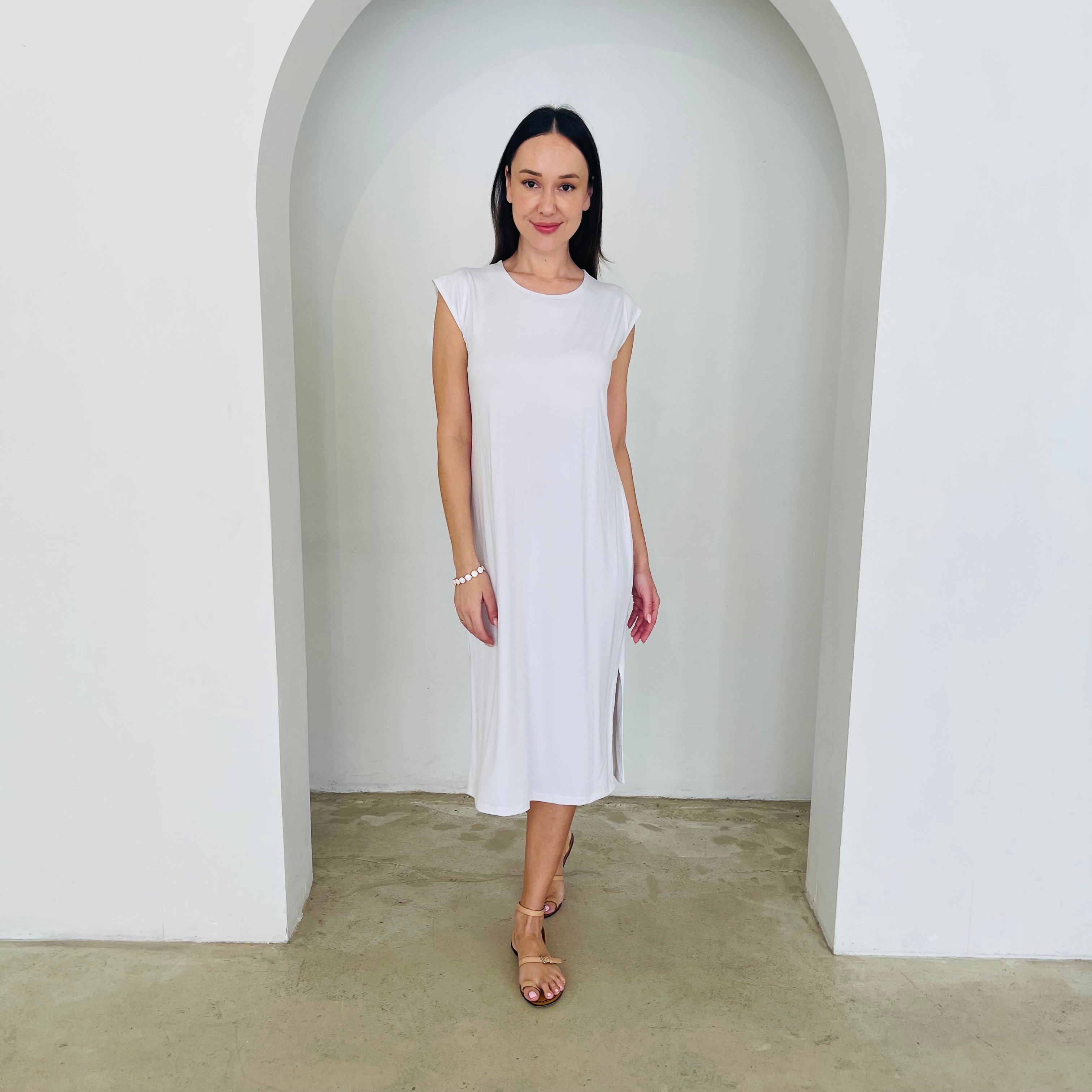 Woman wearing a white dress standing in a minimalistic setting with a white archway.