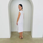 Woman wearing a white dress standing in a minimalistic setting with a white archway.