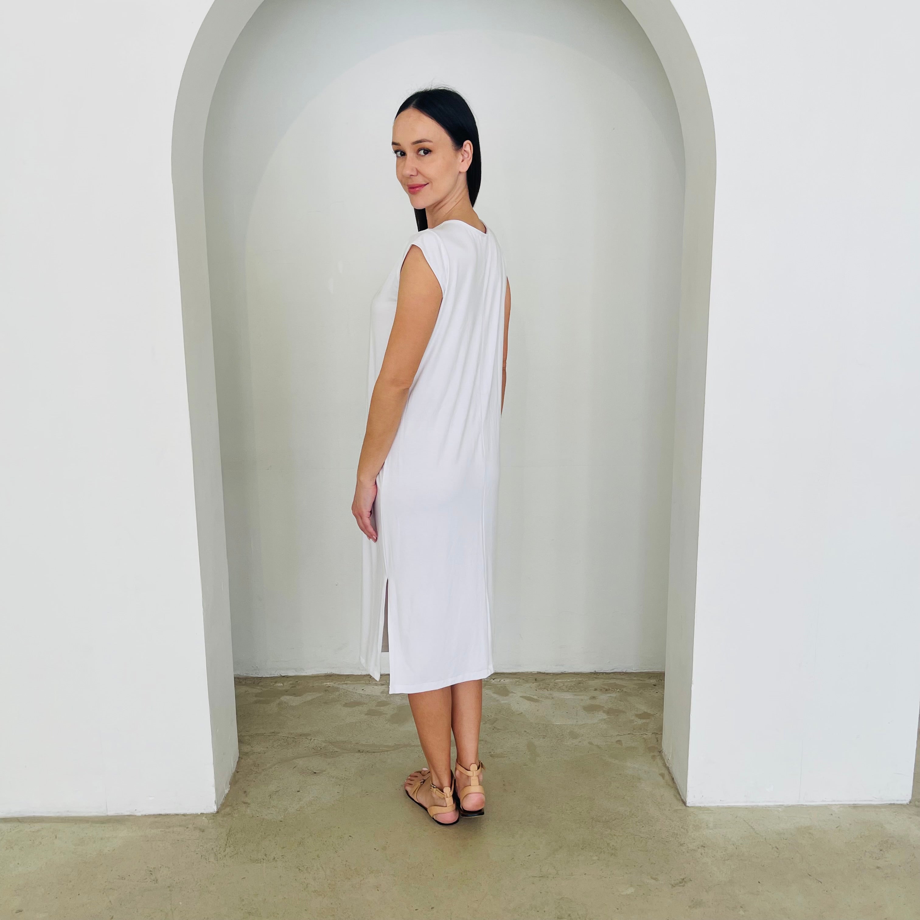Woman wearing a white dress standing in a minimalistic setting with a white archway.