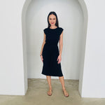 Woman wearing a black dress standing in a white archway.