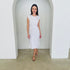 Woman wearing a white dress standing in a minimalistic room with white walls and a concrete floor.