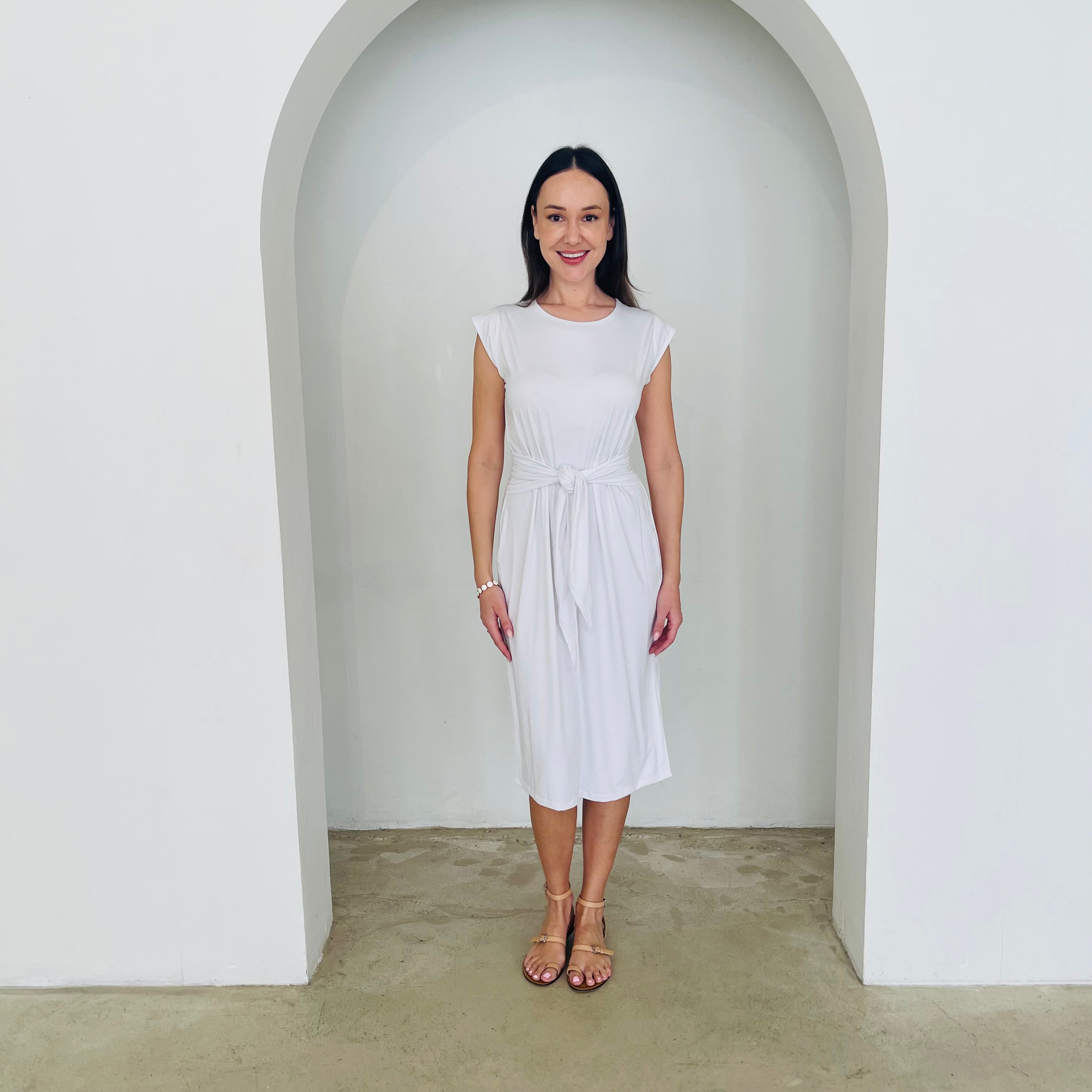 Woman in a white dress standing in a white archway.