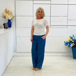 Woman wearing white dressy top, and jeans, standing in a room with white walls and decorative elements.