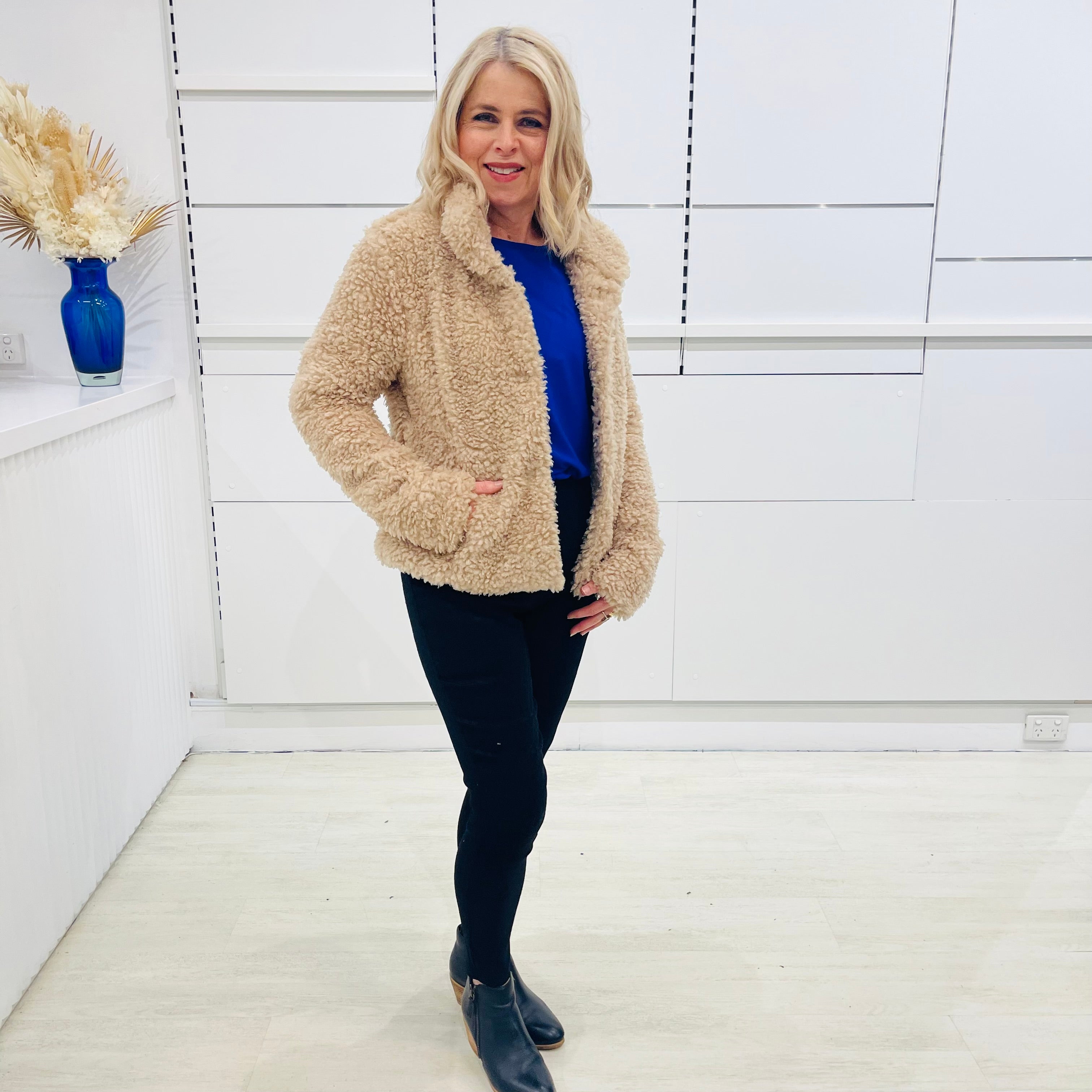 Tan fluffy, faux fur, teddy bear, Bailey Jacket, with pockets, worn with tailored fitted black pants and cobalt blue, relaxed fit, bamboo top. 