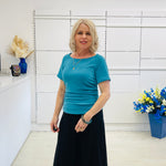 Woman in a blue top and black skirt standing in a room with white walls and decorative elements.