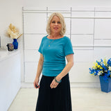 Woman in a blue top and black skirt standing in a room with white walls and decorative elements.