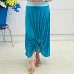 Person wearing a blue skirt with a knot detail on a white floor.
