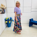 Woman in a colorful skirt and purple top standing in a room with decorative elements.