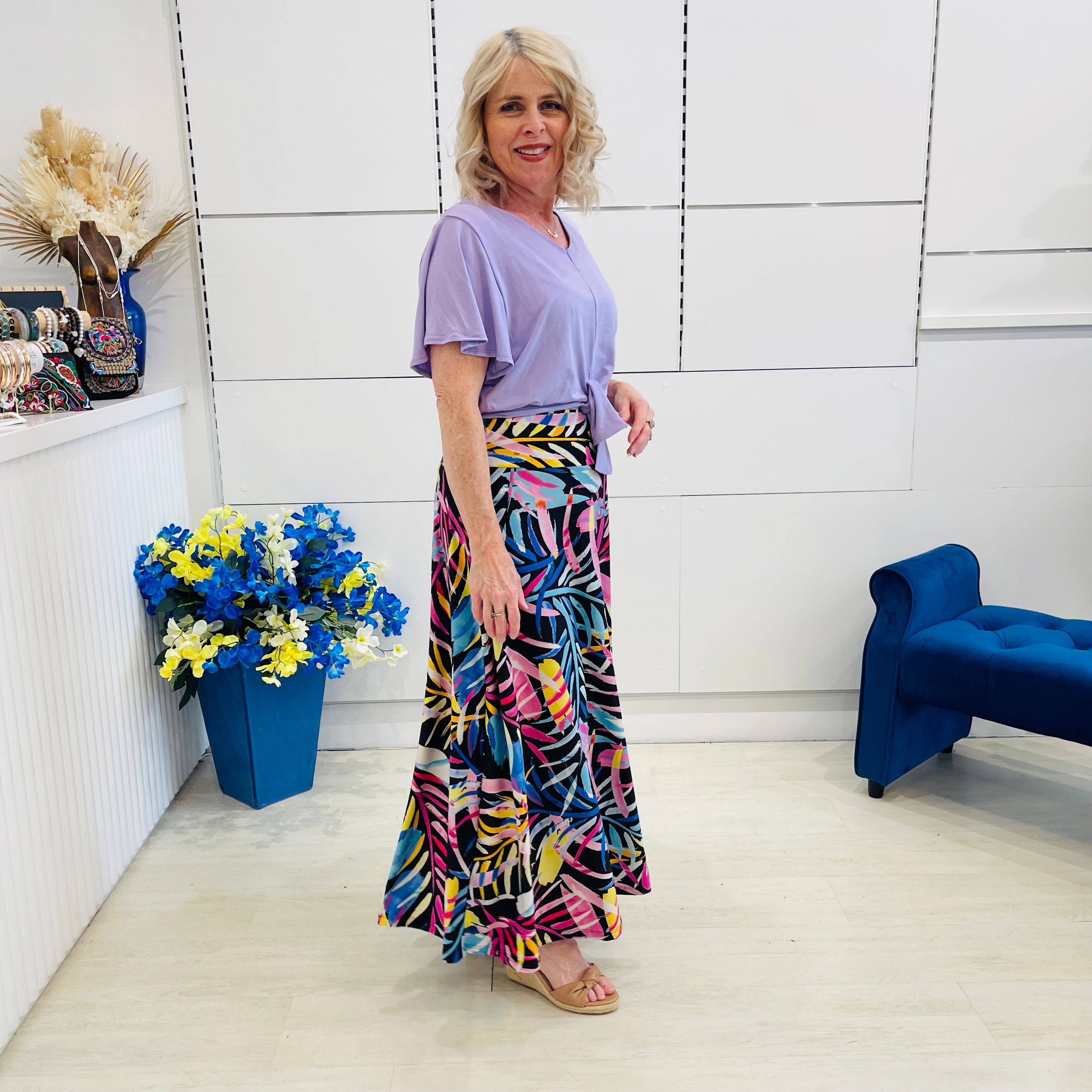 Woman in a colorful skirt and purple top standing in a room with decorative elements.