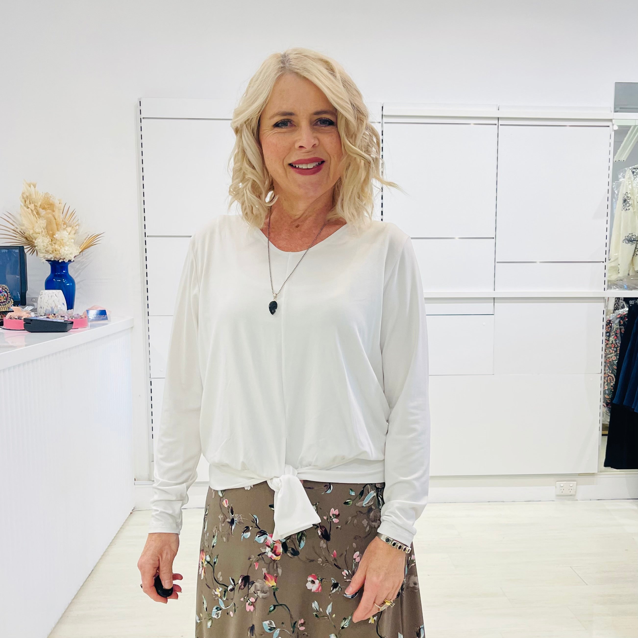 White long sleeve, v neckline, top with waist tie front, worn with floral, midi length skirt.