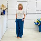 Woman wearing a white top and blue pants standing in a room with white walls and decorative elements.