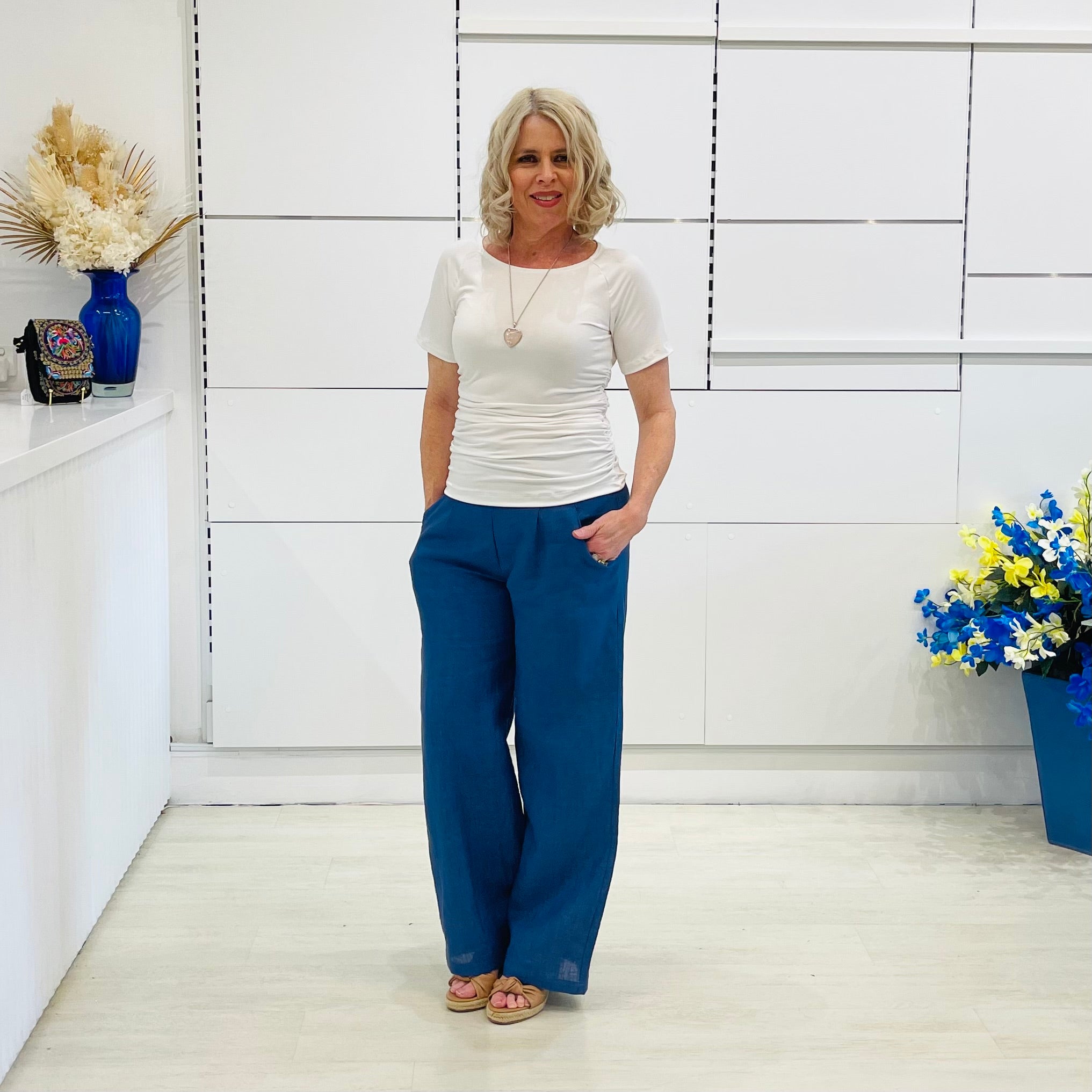 Woman wearing a white top and blue pants standing in a room with white walls and decorative elements.
