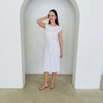 Woman wearing a white dress standing in a minimalistic setting with a white archway.