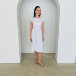 Woman wearing a white dress standing in a minimalistic room with a white archway.