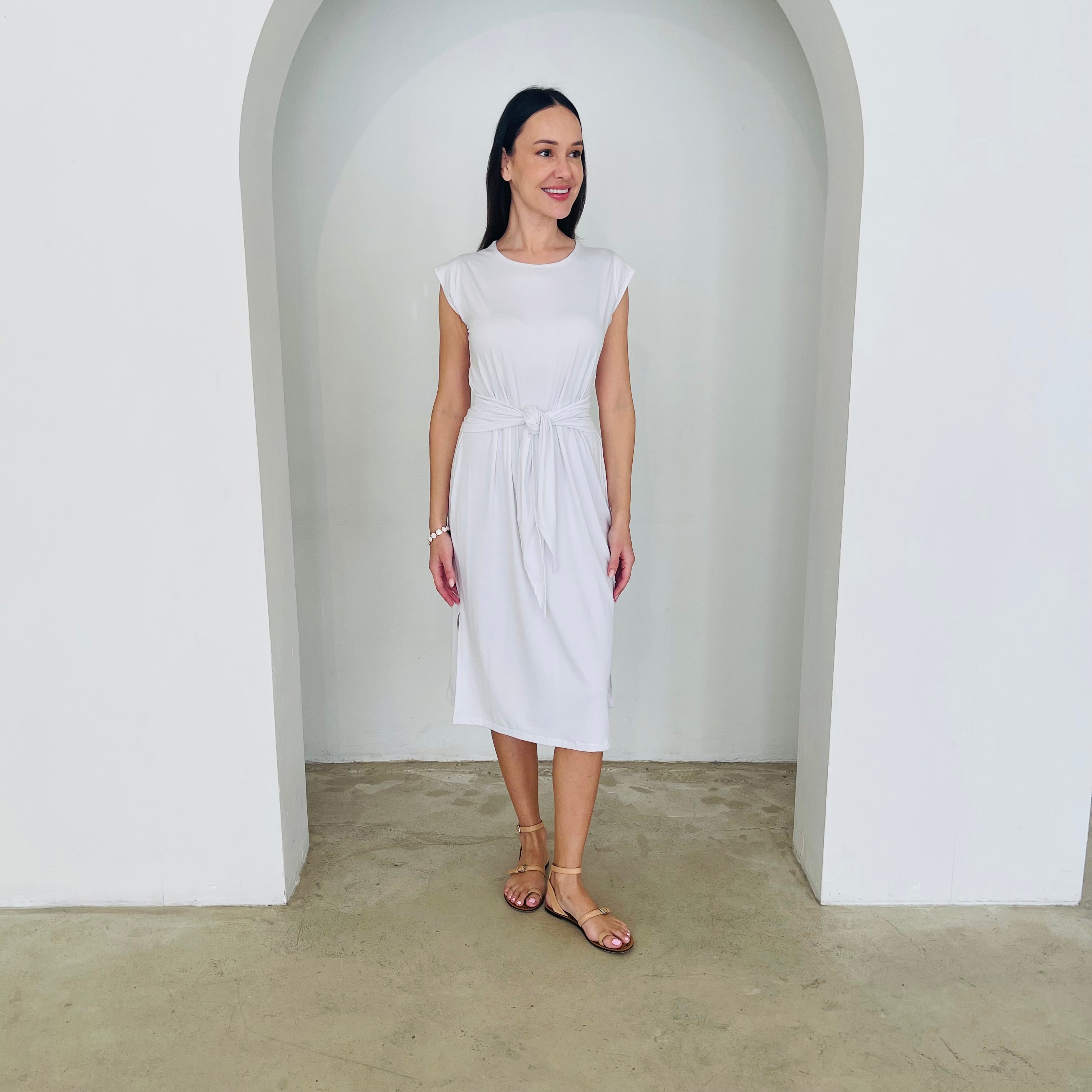 Woman wearing a white dress standing in a minimalistic room with a white archway.