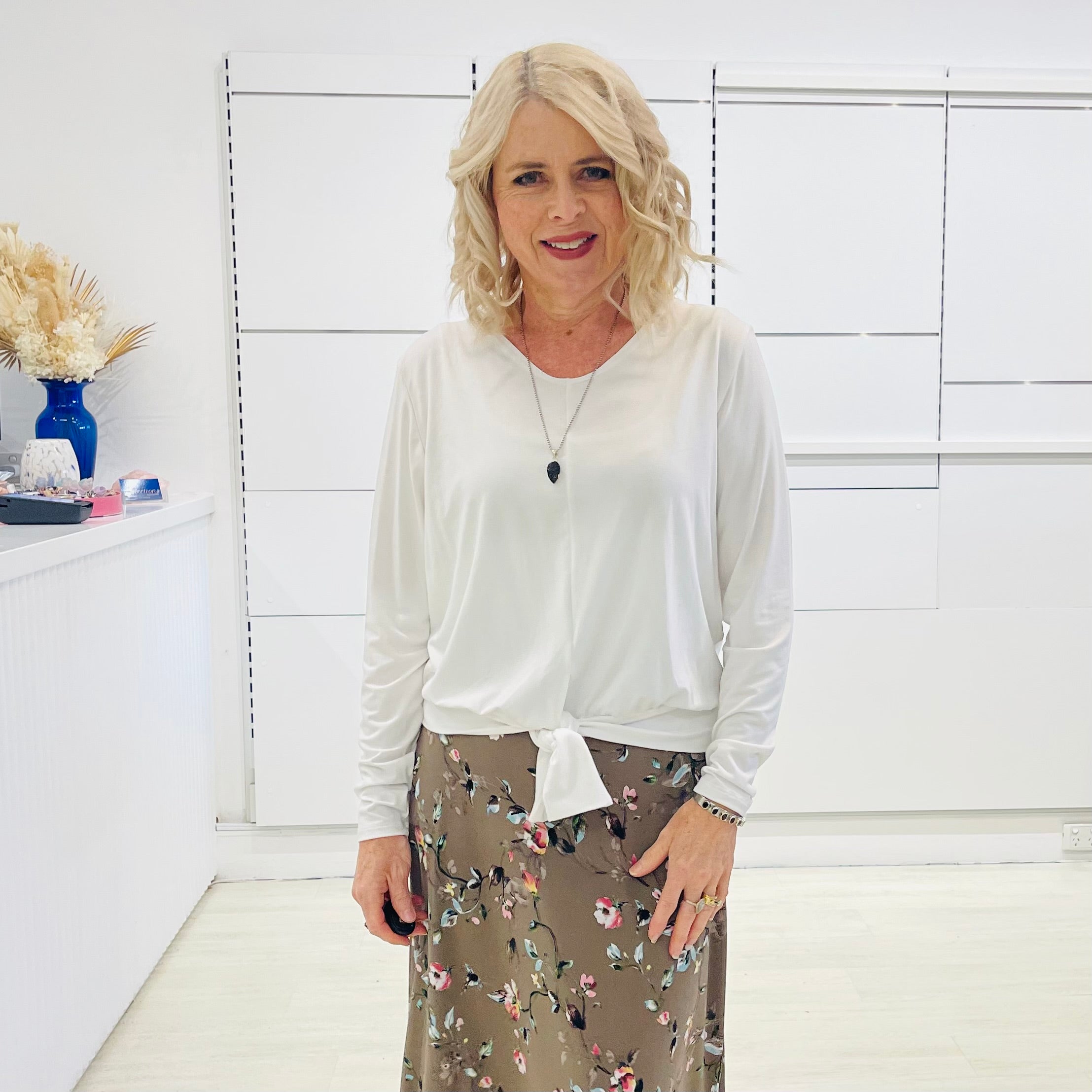 White long sleeve, v neckline, top with waist tie front, worn with floral, midi length skirt.