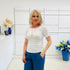 Woman wearing a white t-shirt and blue pants standing in a room with white walls and decorative elements.