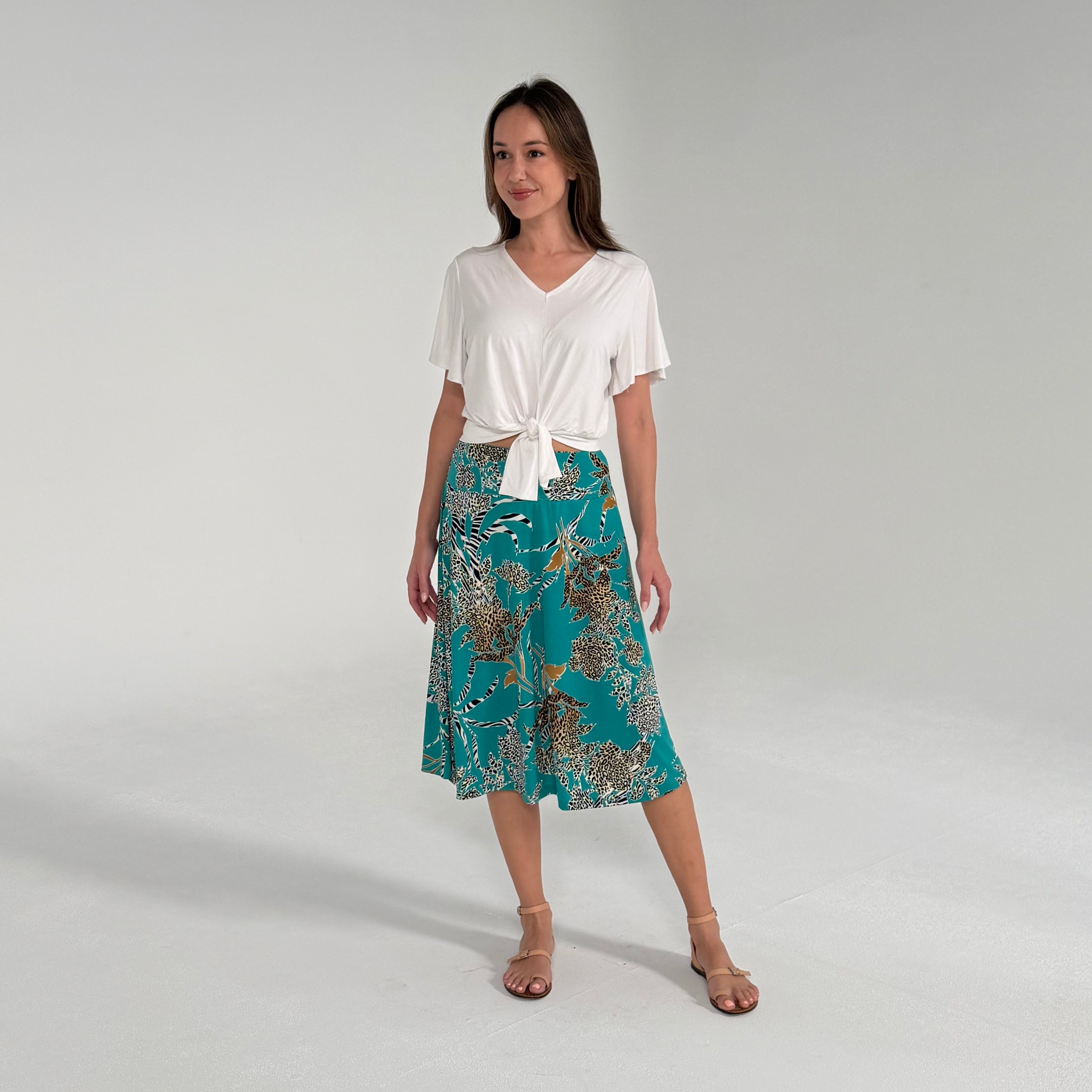 Woman wearing a white top and teal patterned skirt on a plain background