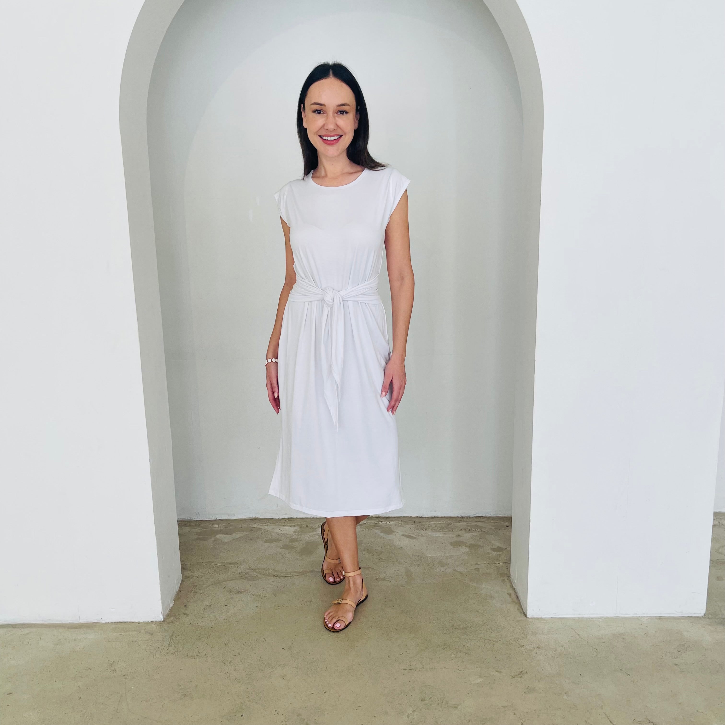 Woman wearing a white dress standing in a minimalistic setting with white arches.