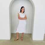 Woman in a white dress standing in a minimalistic setting with an archway.