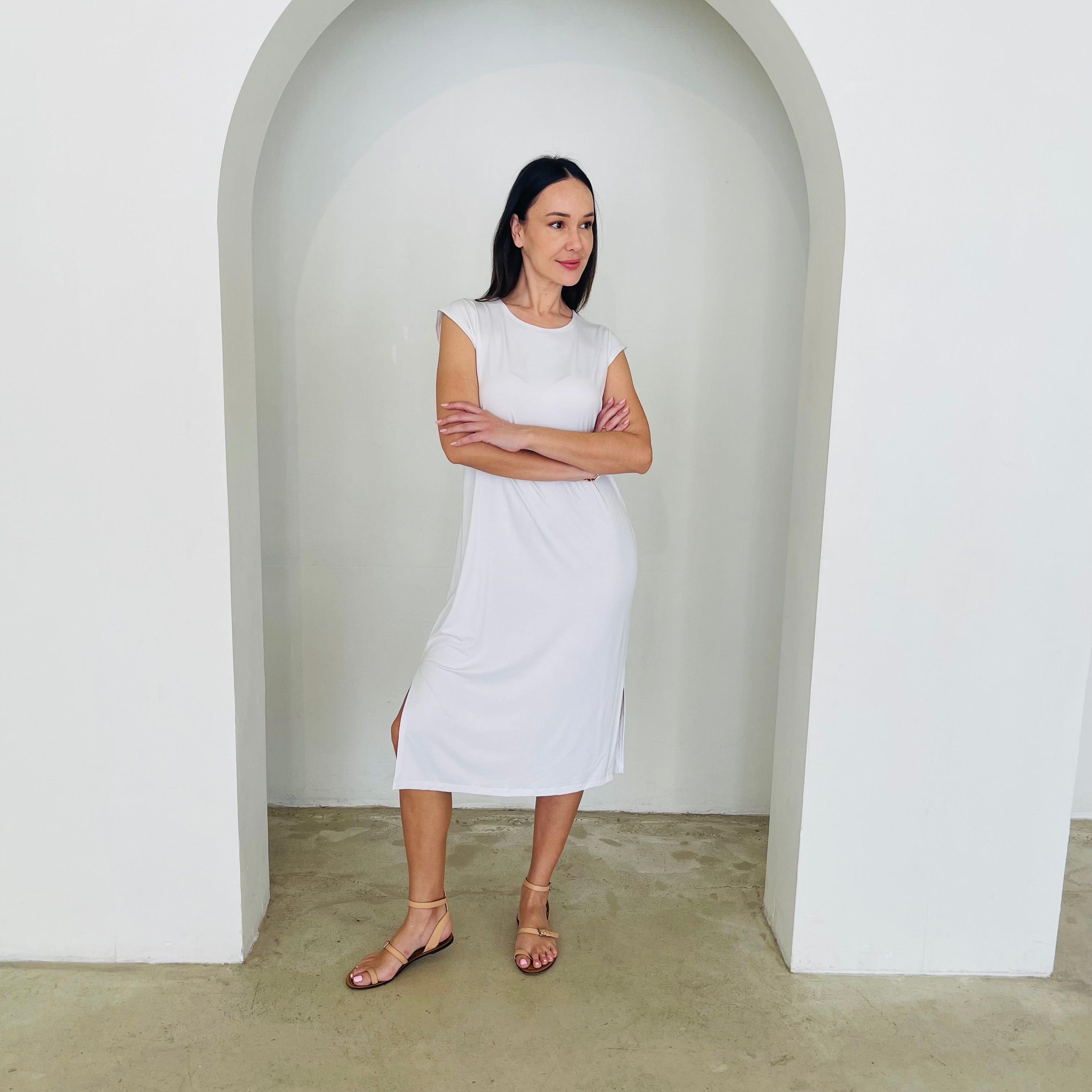 Woman in a white dress standing in a minimalistic setting with an archway.