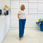 Woman in a white top and blue pants standing in a room with white walls and decorative elements.