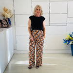 Woman wearing a black top and patterned pants standing in a modern room with decorative elements.