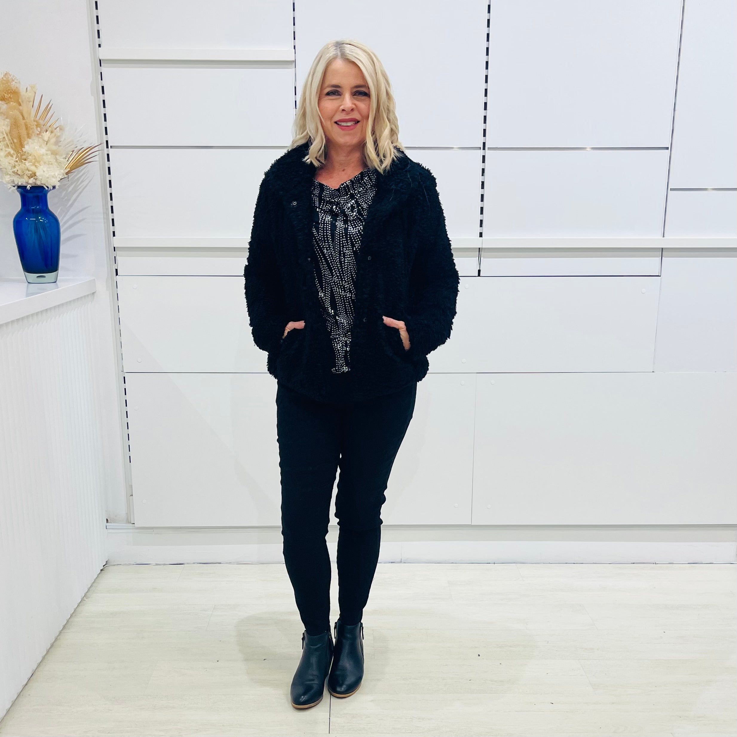 Black fluffy, faux fur, teddy bear jacket with pockets. Worn with black tailored fitted pants and a black and silver sparkly cowl neckline top. 