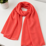 Coral-colored scarf on a white surface with a plant in the background