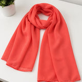 Coral-colored scarf on a white surface with a plant in the background