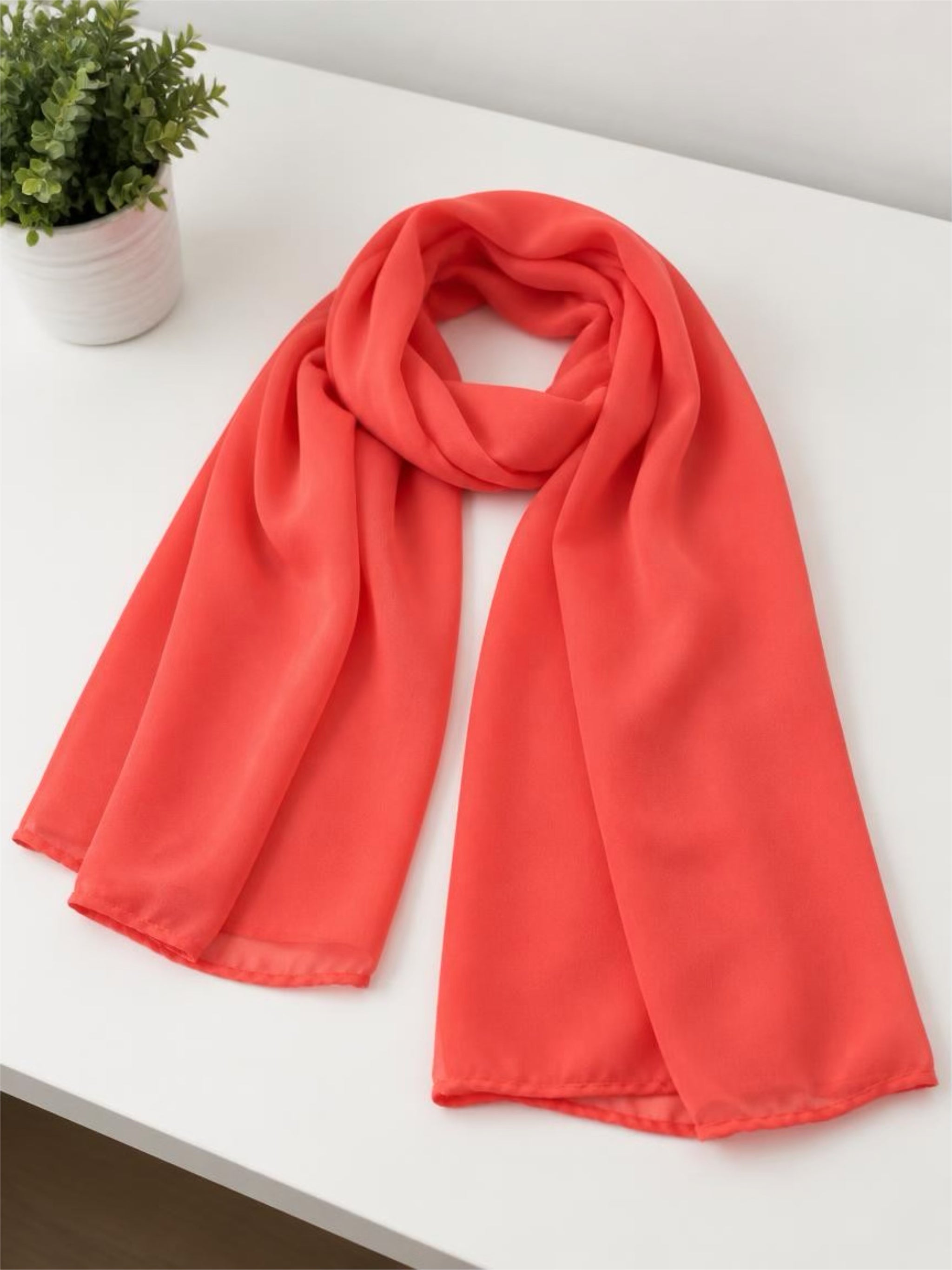 Coral-colored scarf on a white surface with a plant in the background