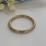 Gold bracelet bangle on a white surface with flowers in the background