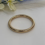 Gold bracelet bangle on a white surface with flowers in the background