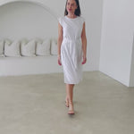 Woman in white dress with belt walking around simple room 