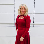 Close up, front view. Woman wearing the Penelope dress n rich ruby red, featuring a fit-and-flare, knee length, slihouette, full length sleeves, and a cut out neckline.
